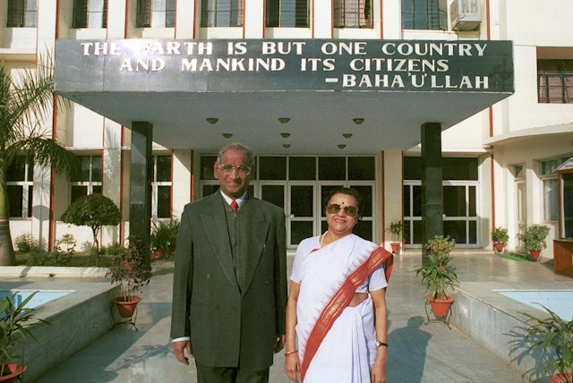 Jagdish Gandhi and Bharti Gandhi, founders of the City Montessori School in Lucknow, India.| They are standing in front of the main building of Gomti Nagar branch of the School, one of 20 branches in Lucknow. A quote from Baháâuâlláh, "The earth is but one country and mankind its citizens" is on the awning behind them.